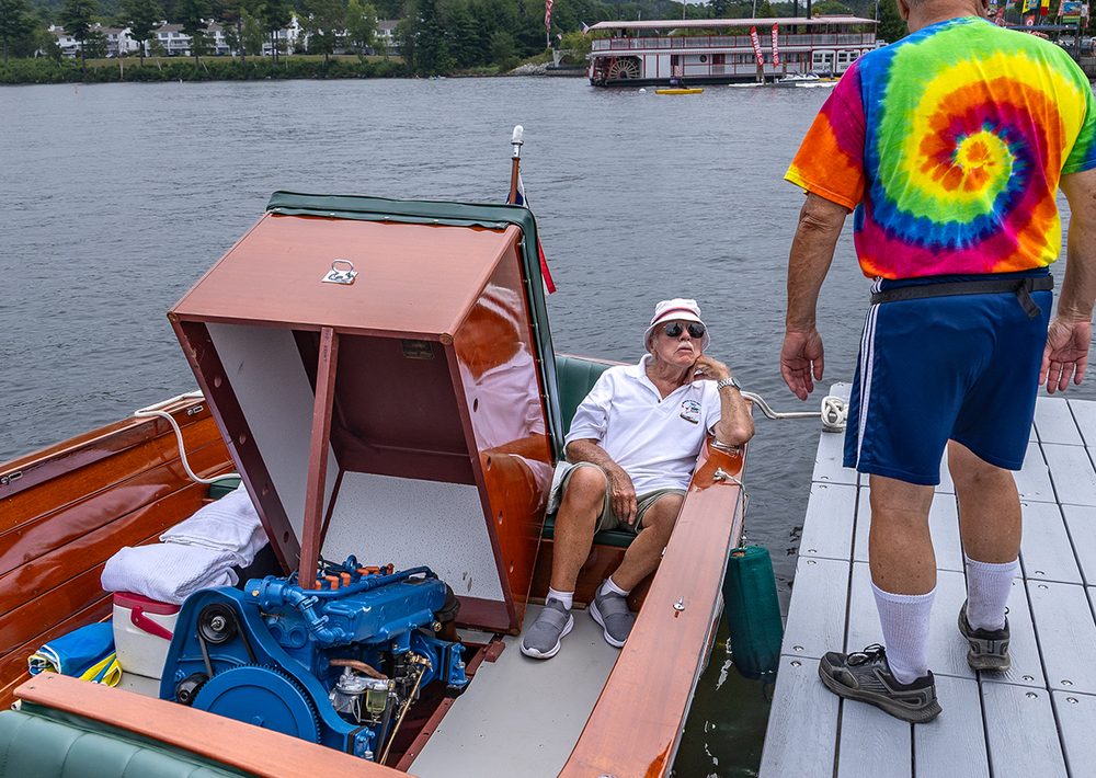 A boat owner seated in his classic runabout chatting with a visitor on the dock